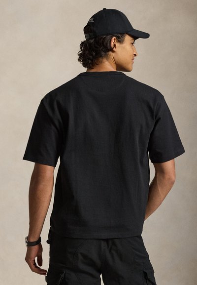 Μαύρο βαμβακερό μπλουζάκι με κοντά μανίκια, λαιμόκοψη crew και άνετη εφαρμογή. Η πίσω πλευρά είναι απλή, χωρίς διακοσμητικά στοιχεία.