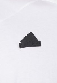 Czarna łatka logo Adidas z trzema paskami i tekstem na białym tle.