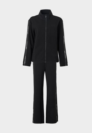 Črn trenirko, sestavljen iz jopice z zadrgo in zvonasto razširjenih hlač. Poudarki s logotipom in belimi stranskimi črtami. Iz mehkega, teksturiranega blaga.