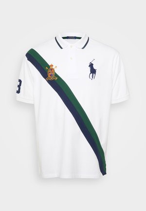 Camisola polo branca com uma faixa diagonal verde e azul-marinho. Apresenta um emblema bordado e o número "3" na manga, com um design de colarinho clássico.