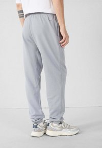 Lichtgrijze sweatpants met een elastische tailleband, zijzakken en een losse pasvorm. Draag ze met grijze en zilveren sportschoenen.