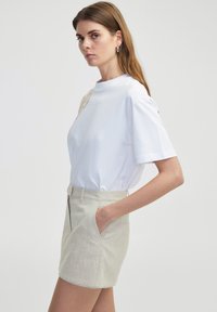 Chemise blanche à manches courtes avec des détails texturés, associée à un short en lin beige présentant des poches latérales et une coupe ajustée.