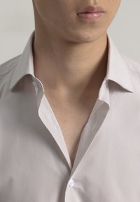 Camisa a rayas beige claro con cuello tipo spread, que presenta una parte frontal abotonada y una textura suave, visible en el escote y la parte superior del torso.