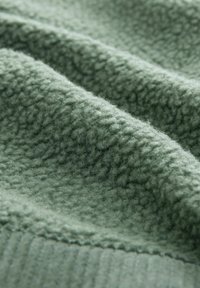 Tissu polaire vert clair doux avec une surface texturée et duveteuse et un bord côtelé visible en gros plan.