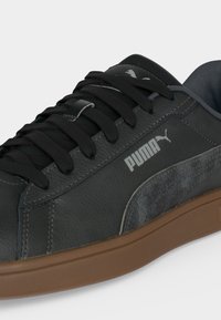 Μαύρο δερμάτινο αθλητικό παπούτσι Puma με μαύρα κορδόνια, γκρι λεπτομέρεια από σουέτ στο πλάι, λευκό λογότυπο Puma και καφέ λαστιχένια σόλα.