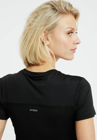 Čierne športové tričko s krátkymi rukávmi, ktoré má textúrovaný vzor a logo na chrbte. Hladká tkanina s priliehavým strihom.