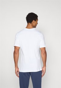 Hvid t-shirt med korte ærmer og rund halsudskæring, lavet af et glat materiale. Har en afslappet pasform og et enkelt design uden synlige logoer.