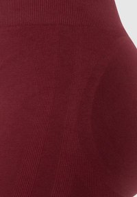 Bordeaux legging met ribbel- en textuurpatronen, met gladde en contrasterende panelen voor extra detail en ontwerp.