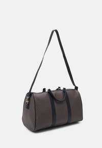Sac de voyage à motif marron en matériau synthétique. Équipé de quincaillerie dorée, de deux poignées supérieures et d'une bandoulière réglable.