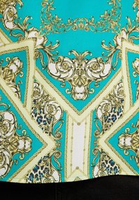 Top turquesa con patrones dorados ornamentales y acentos de estampado de leopardo, con un diseño geométrico que presenta secciones blancas en contraste. Textura suave.