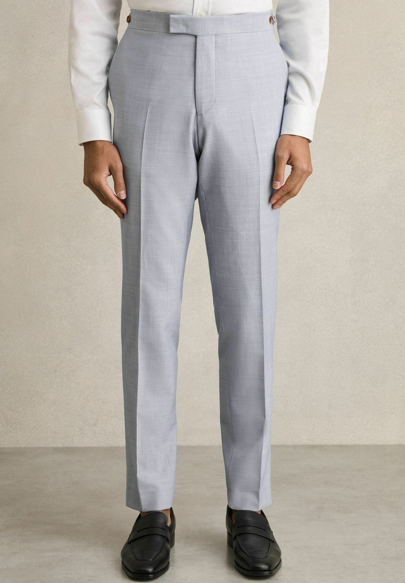 Pantaloni gri deschis, croiți, cu o textură netedă, având pliuri ascuțite, picioare drepte și un design frontal plat. Împărțiți cu loaferi negri.