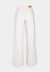 Jeans brancos de perna larga feitos de algodão com uma textura lisa, apresentando uma cintura alta, grandes bolsos traseiros e um rótulo castanho na cintura.