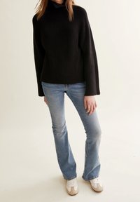 Svart ribbad stickad tröja med hög krage, ihopparad med ljusblå utsvängda jeans och vita sneakers med beige detaljer.