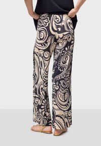 Breda byxor i en krämfärgad tyg med svart paisleymönster. Mjuk textur, elastisk midja och avslappnad passform, kompletterat med metallicsandaler.
