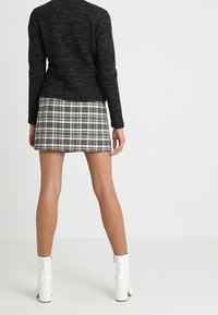 Maglione nero a trama abbinato a una mini gonna scozzese nei toni del verde e del beige. Stivaletti bianchi con tacco completano l'outfit.