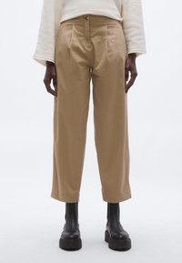 Bézs magasderekú nadrág elöl hajtásokkal, egyenes szárú és rövidített hosszúságú, fekete vastag talpú bokacsizmával párosítva.