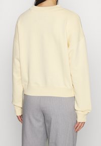 Sweatshirt couleur crème avec une coupe décontractée, poignets et ourlet côtelés. Tissu doux et lisse avec un col ras du cou classique.