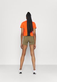 Camiseta naranja cortada con panel trasero negro, combinada con pantalones cortos verde oliva. El modelo lleva zapatillas deportivas blancas. Diseño de ropa deportiva simple y funcional.