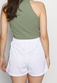 Green sleeveless top with a crew neck, paired with white shorts featuring black side stripes and an elastic waistband.