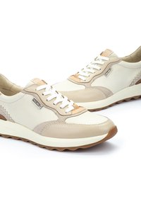 Zapatillas de cuero beige con cordones y detalles blancos. Las características incluyen un acabado texturizado, secciones en contraste de color marrón y una suela acolchada.