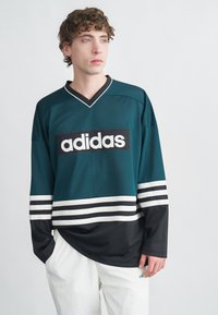 Türkiz hálós sportmez fekete-fehér csíkos szegéllyel és ujjakkal; a mellkason jól látható fehér "adidas" logó.