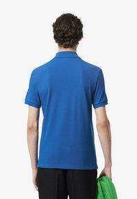 Camisa polo azul de manga corta con cuello plano, hecha de tela suave, con un dobladillo recto. Combinada con pantalones negros y tela verde.