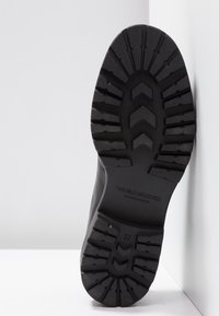 Semelle en caoutchouc noir avec surface texturée, présentant des motifs en zigzag et en lignes pour l'adhérence, logo embossé et numéro de taille 37.