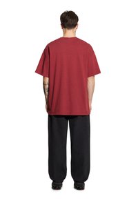 Bordowa bawełniana koszulka wyświetlana z tyłu, z krótkimi rękawami i luźnym krojem, zestawiona z czarnymi luźnymi spodniami.
