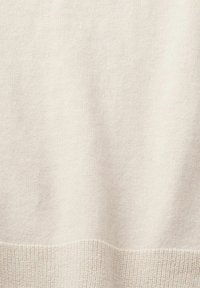 Tessuto lavorato a maglia di un beige chiaro con una morbida texture. Presenta un orlo leggermente a coste nella parte inferiore, creando un aspetto liscio e continuo.