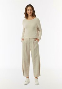 Beżowy sweter dzianinowy o luźnym kroju i okrągłym dekolcie, w zestawieniu z beżowymi spodniami o wysokim stanie z bocznymi kieszeniami i guzikami.