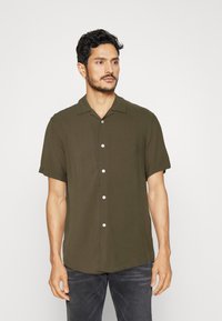 Chemise vert olive à manches courtes avec un devant boutonné, un col pointu et une coupe décontractée. Le tissu semble lisse et léger.