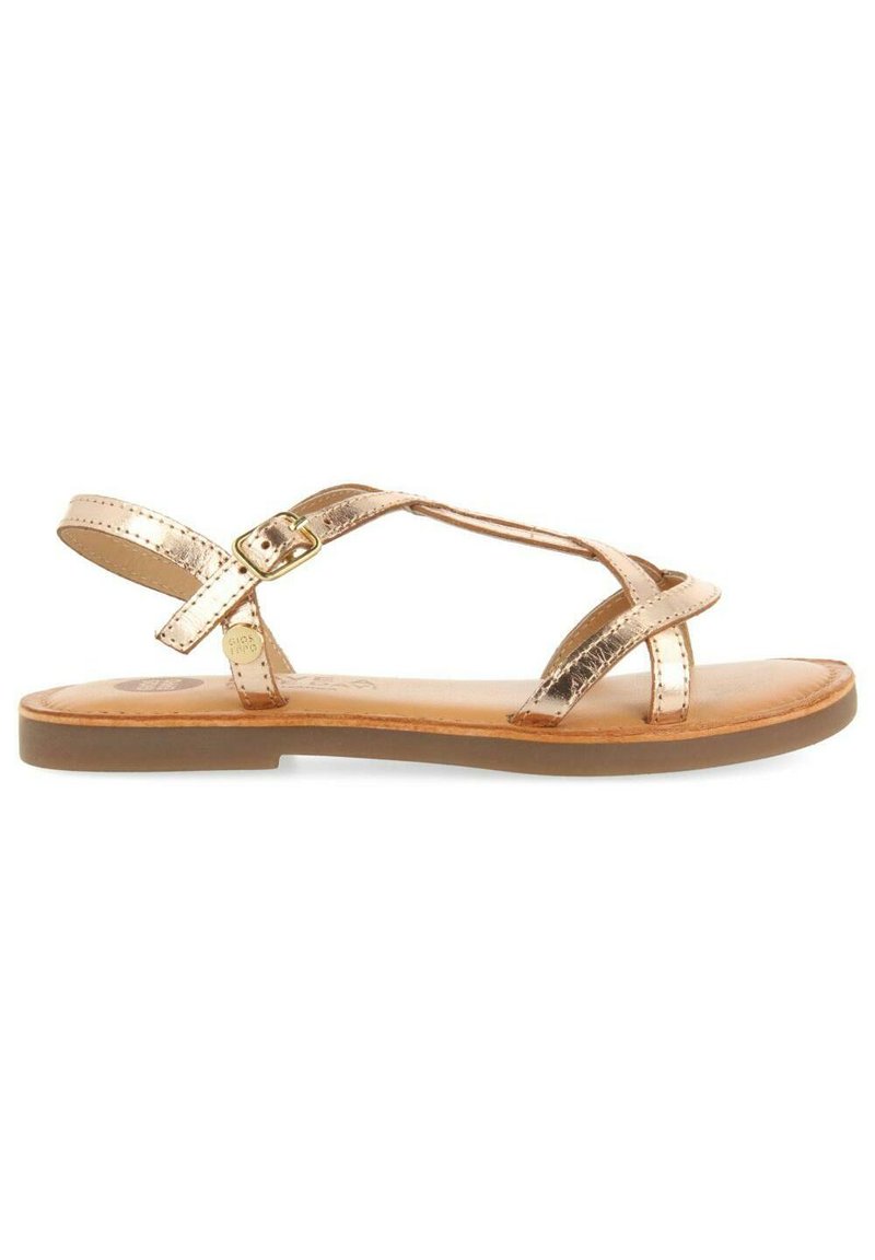 Sandali metallici color bronzo con multiple cinghie incrociate, fibbia regolabile alla caviglia e suola piatta marrone. Texture in pelle liscia.