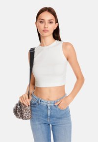 White, sleeveless crop top with a crew neckline paired with light blue high-waisted jeans. Accessories include a small leopard print bag.