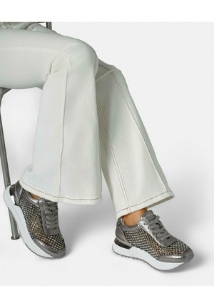 Nogi skrzyżowane, ubrane w białe rozszerzane spodnie oraz metaliczno-szare trampki z ozdobami z kryształków i białymi podeszwami.