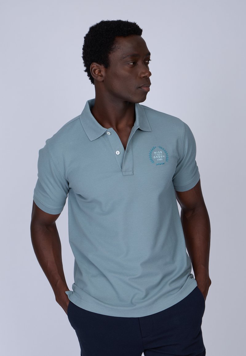 Polo shirt bleu clair en coton, doté d'un col côtelé, de manches courtes et d'un logo avant en bleu plus foncé. Design ajusté.