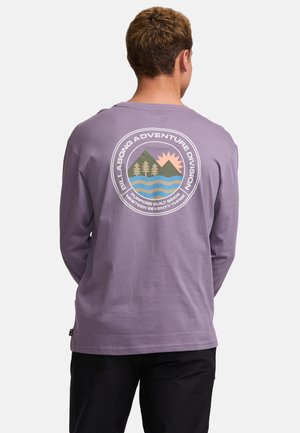 Pitkähihaisen purppuranvärisen T-paidan materiaalina on puuvilla, ja siinä on pyöreä graafinen kuvasto, jossa on vuoria, aurinko ja vettä. Paidassa on brändi "Billabong Adventure Division".
