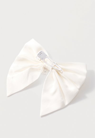 Barrette à cheveux en tissu blanc avec fermoir en métal argenté sur un fond gris clair.