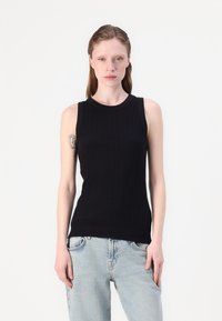 Svart ribbet tropsløse topp med rund hals, med en tettsittende design. Kombinert med lyseblå, avslappede jeans.