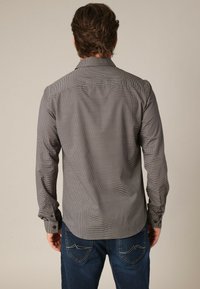 Grijs patroon langwerpig overhemd met een kraag, knoopmanchetten en een subtiel textuur. Gecombineerd met blauwe jeans.