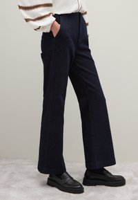 Marineblaue, hoch taillierte Jeanshose mit geradem Bein und seitlichen Taschen, kombiniert mit schwarzen Loafers.