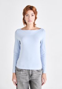 Lys blå langermet topp med bred båthals, laget av glatt stoff. Brukt sammen med grå, ledige jeans med klassisk lommedesign.
