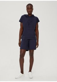 Dunkelblauer Kapuzenpullover mit einem strukturierten Blättergrafik und einer Tasche, kombiniert mit passenden Shorts. Weiße Sneaker vervollständigen das Outfit.