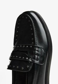 Fekete bőrből készült mokaszin díszítő pánttal, fém szegecsekkel és kivágással az felső részén. Simább textúrájú, kerek orrú.