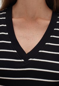 Svart och vit randig ribbad topp med V-ringning. Tyget har en texturerad yta med växelvis horisontella ränder.