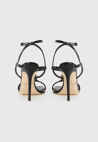 Μαύρα ψηλοτάκουνα σανδάλια από δέρμα με λεπτά λουράκια, μυτερή μύτη και τακούνι στιλέτο. Διαθέτουν ταμπά εσωτερική σόλα και κούμπωμα στον αστράγαλο.