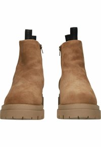 Botas de tobillo de ante en color marrón con una suela gruesa y texturizada y cremallera lateral. Presentan una lengüeta con el logotipo de la marca en la parte posterior.