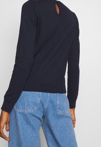 Marinblå stickad tröja med detalj i form av nyckelhål bak, figurnära ärmslut och ribbad nederkant, kombinerad med ljusblå jeans med hög midja.