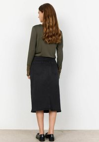 Svart denim midi kjol med en åtsittande midja, bakfickor och rå kant. Kombinerad med en olivgrön långärmad topp med spetsdetaljer.