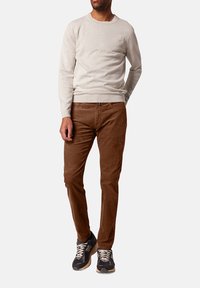 Lichtgrijze crew-neck trui, bruine corduroy broek en donkere sneakers. De outfit heeft een casual ontwerp, met ribbels bij de mouwen en tailleband.
