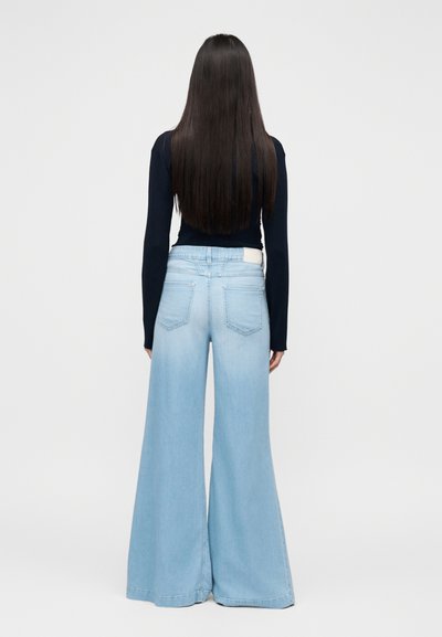 Φαρδιά τζιν παντελόνια σε ανοιχτό μπλε χρώμα με ψηλή μέση, ξεβαμμένο πλύσιμο και δύο τσέπες στο πίσω μέρος. Συνδυασμένα με εφαρμοστό μακρυμάνικο μπλε τοπ.